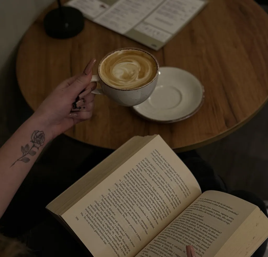 A cup of cappuccino and an open book on a wooden table