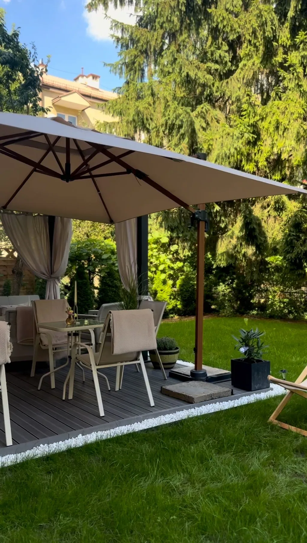 The garden decking under a large parasol, with lawn and planters alongside